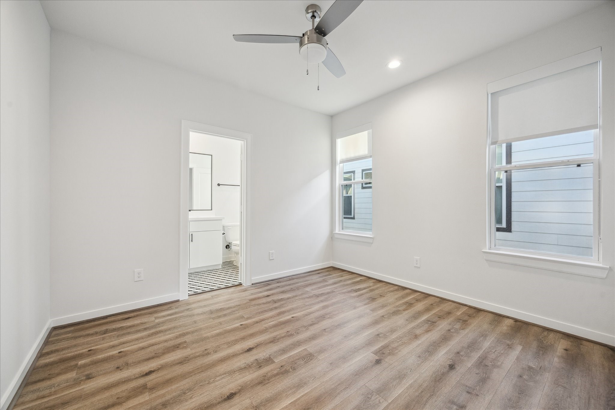 1603 Patterson Street, Unit E Houston, TX 77007 - Photo 23 of 32 This room features a modern design with light wood flooring and neutral walls. It includes a ceiling fan and two large windows for natural light. An ensuite bathroom with contemporary fixtures is accessible through an open doorway.