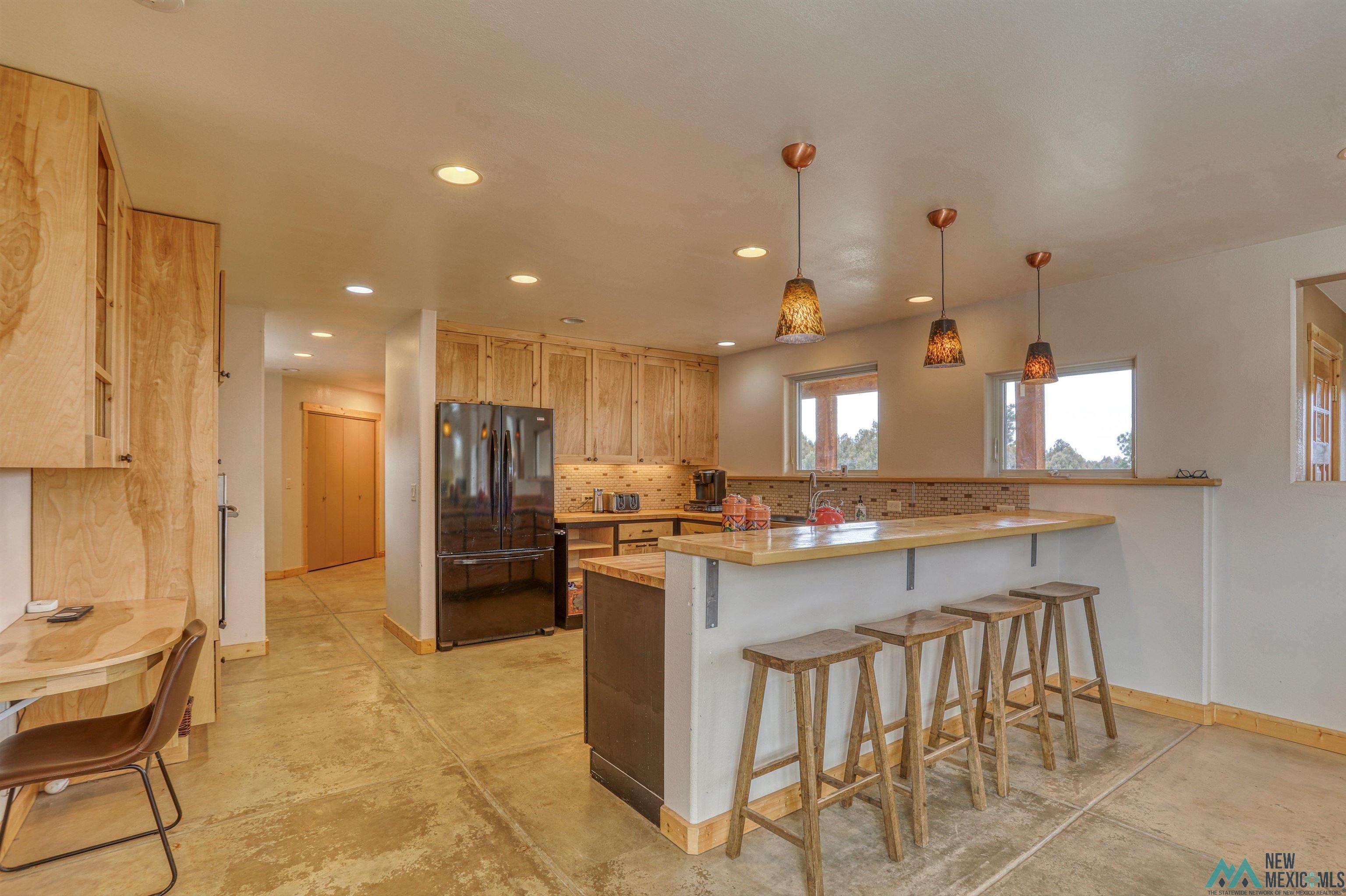 12 Horn Toad Road Chama, NM 87520 - Photo 12 of 52 Kitchen with a peninsula, freestanding refrigerator, hanging light fixtures, a kitchen bar, and concrete floors