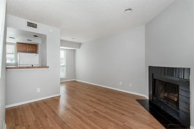 a view of an empty room with wooden floor fireplace and a window