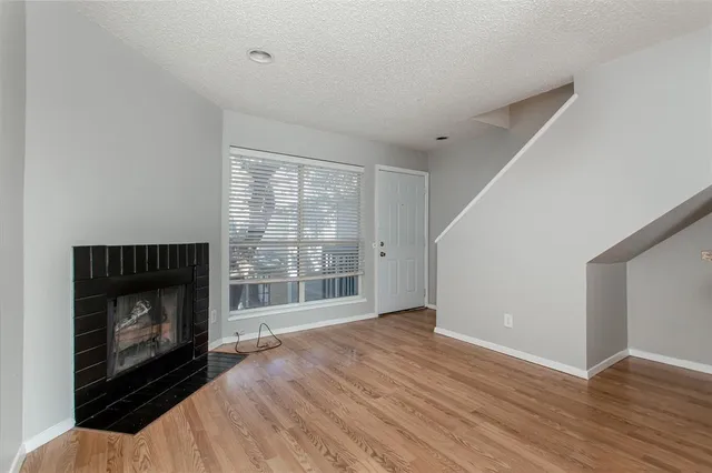 a view of an empty room with wooden floor fireplace and a window