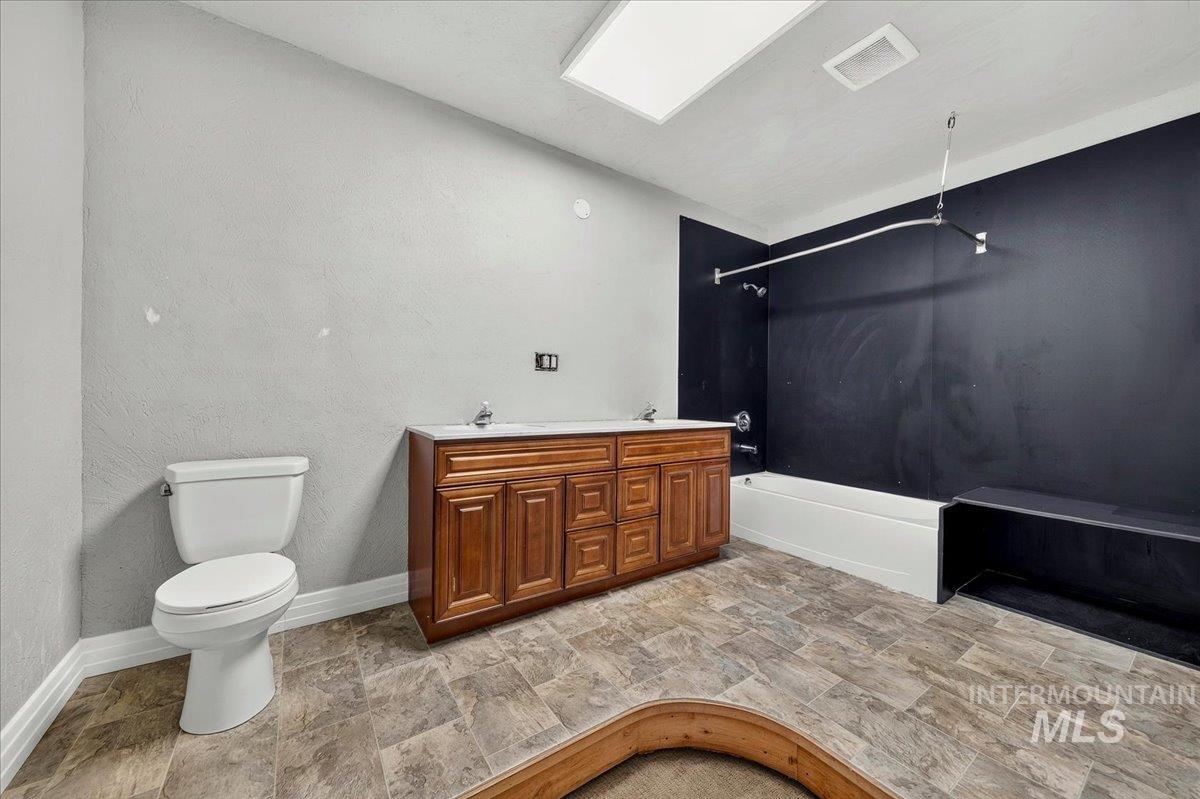 2160 South Five Mile Road Boise, ID 83709 - Photo 34 of 41 Bathroom featuring a double vanity with wood-finish cabinetry and white countertop, a white toilet, and a bathtub with a dark-paneled surround