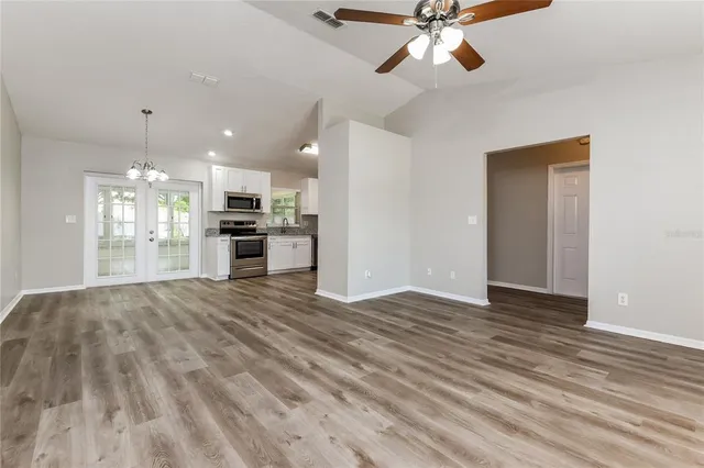 a view of an empty room and kitchen view with wooden floor