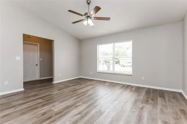 an empty room with wooden floor chandelier fan and windows