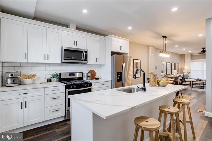 a kitchen with stainless steel appliances kitchen island granite countertop a stove a sink a refrigerator and white cabinets