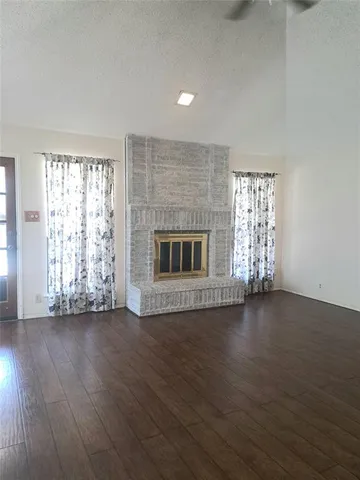 an empty room with wooden floor fireplace and windows