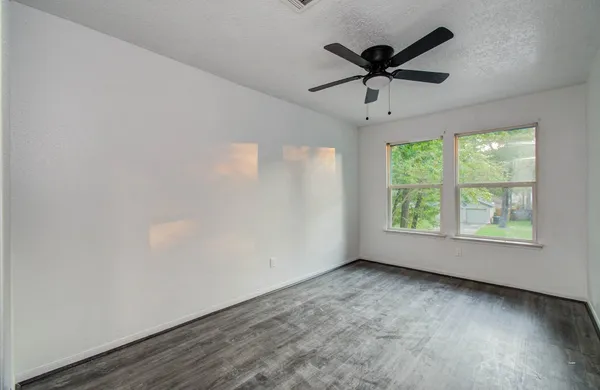 an empty room with wooden floor fan and windows