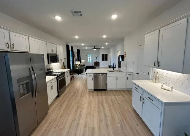 a large kitchen with a large counter top a sink stainless steel appliances and cabinets