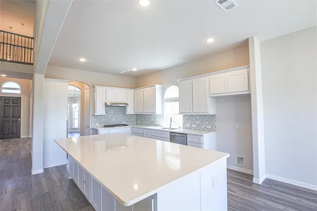 a large kitchen with kitchen island a sink dishwasher a stove and a refrigerator with wooden floor