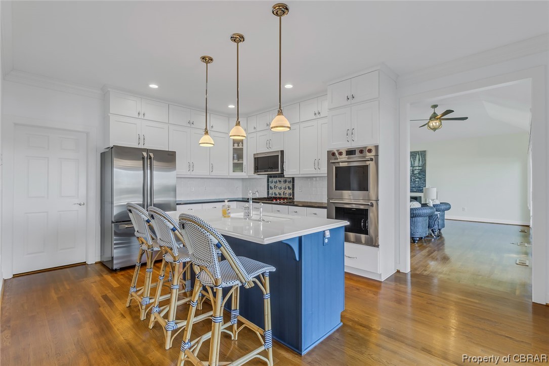 192 Bayberry Point Lane Kilmarnock, VA 22482 - Photo 26 of 49 Kitchen featuring hanging light fixtures, an island with sink, backsplash, white cabinets, light countertops, light hardwood floors, appliances with stainless steel finishes, a center island, and crown molding