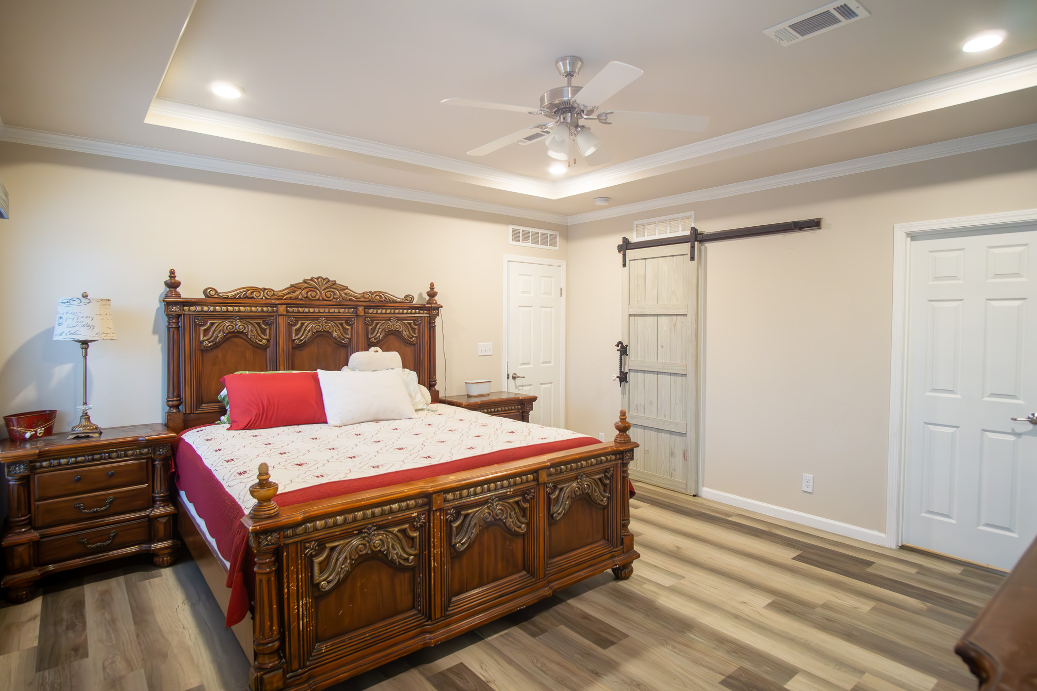 3882 Dry Creek Road Lockhart, TX 78644 - Photo 10 of 34 Bedroom featuring a barn door, wood finished floors, a ceiling fan, ornamental molding, and a tray ceiling