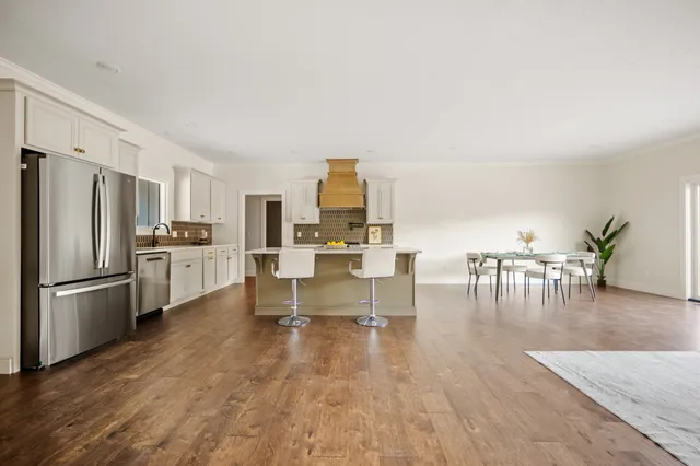 a kitchen with stainless steel appliances a stove a refrigerator a dining table and chairs with wooden floor