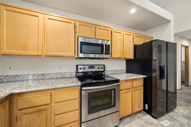 a kitchen with granite countertop a stove top oven microwave and refrigerator