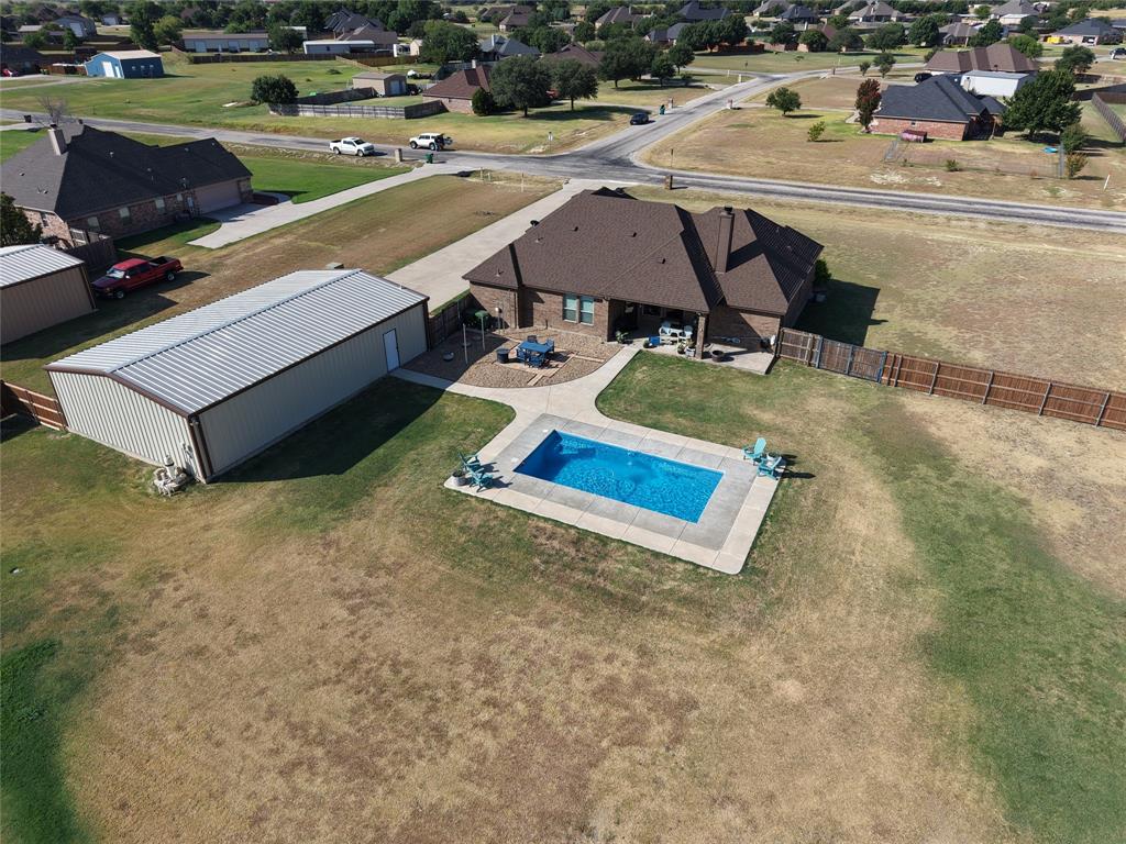 123 Cactus Drive Decatur, TX 76234 - Photo 22 of 30 Expansive rural property featuring a substantial brick residence with covered patio entertaining space, a metal-frame agricultural outbuilding, sparkling in-ground swimming pool with concrete decking, manicured lawn, and mature landscaping.