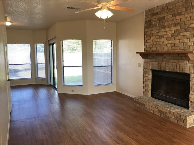 an empty room with wooden floor fireplace and windows