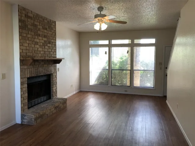 an empty room with wooden floor a chandelier fan and windows