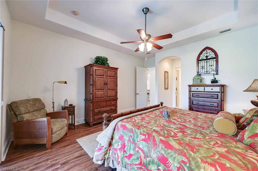 7587 Moorgate Point Way Naples, FL 34113 - Photo 37 of 50 Spacious primary bedroom featuring hardwood flooring, a coffered ceiling with ceiling fan and integrated lighting, custom wood cabinetry, and an en-suite bathroom
