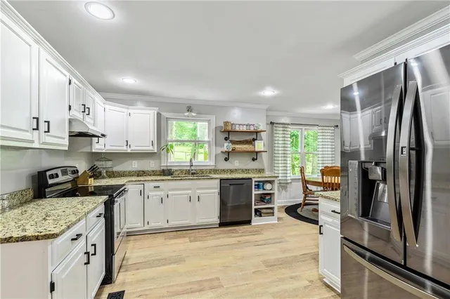 a kitchen with stainless steel appliances granite countertop a stove top oven a sink dishwasher a refrigerator and white cabinets with wooden floor