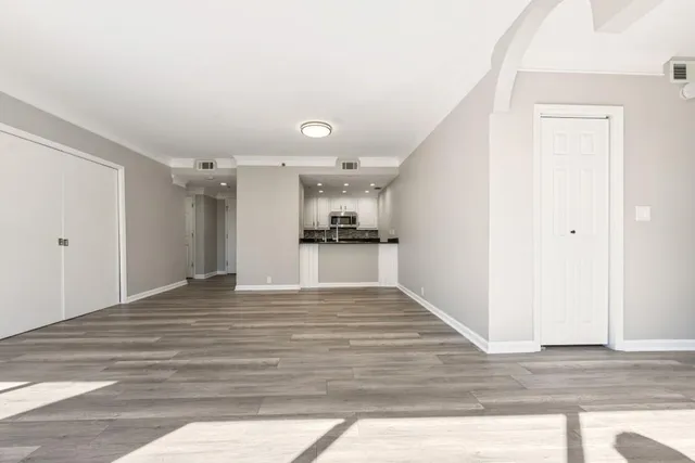 a view of an empty room and kitchen with wooden floor