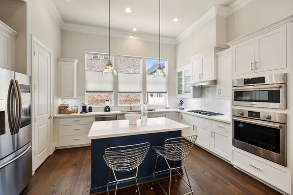 a kitchen with stainless steel appliances granite countertop a stove a sink a microwave a refrigerator and white cabinets with wooden floor