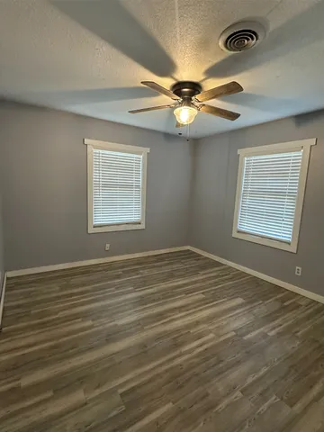 an empty room with wooden floor fan and windows