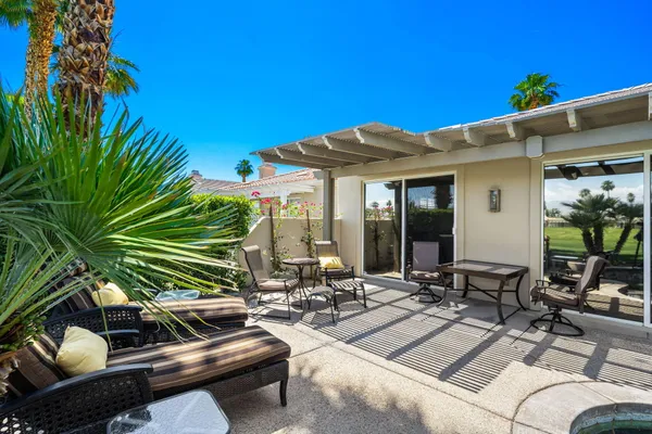 a view of a patio with couches table and chairs under an umbrella with potted plants
