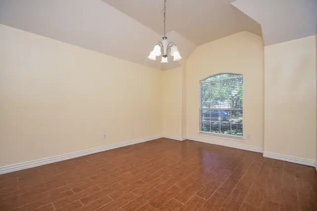 an empty room with wooden floor chandelier and window