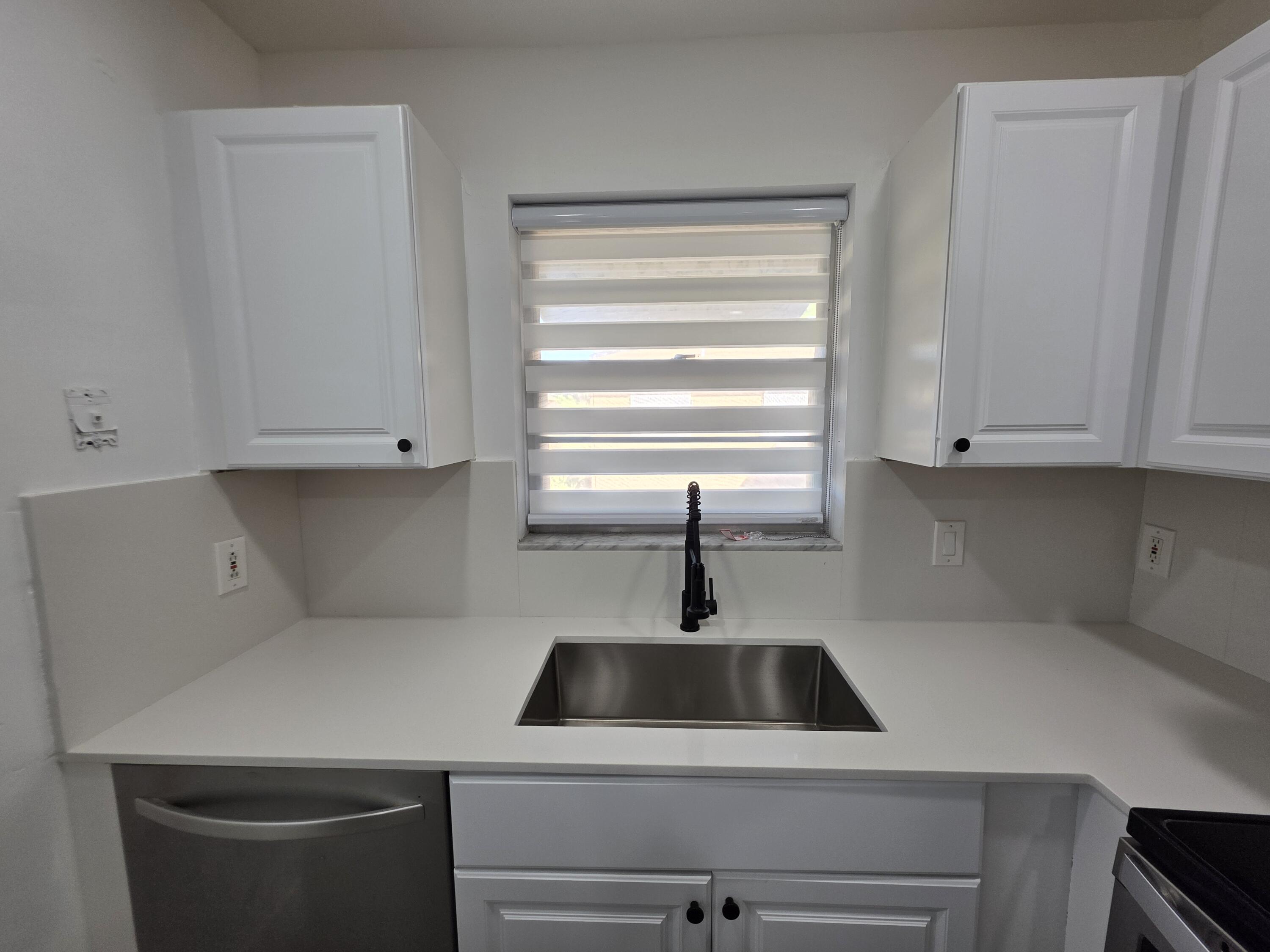 718 Whippoorwill Lane Delray Beach, FL 33445 - Photo 11 of 38 a kitchen with a sink a stove and white cabinets