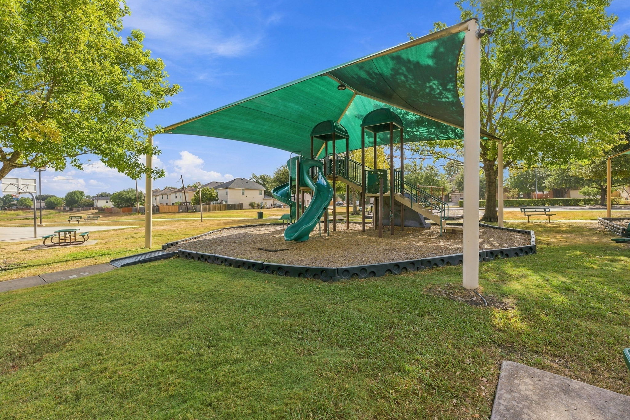 9004 Wiley Way Austin, TX 78747 - Photo 34 of 39 A shaded playground structure sits in a grassy park area surrounded by mature trees.