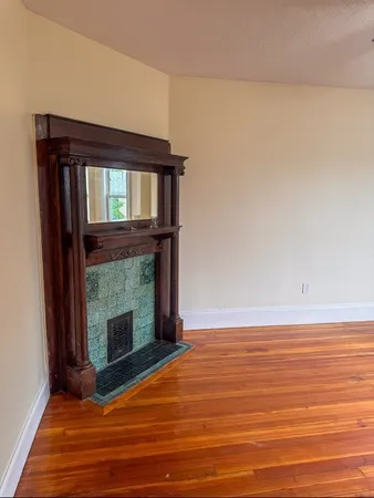 a view of an empty room with wooden floor fireplace and a window