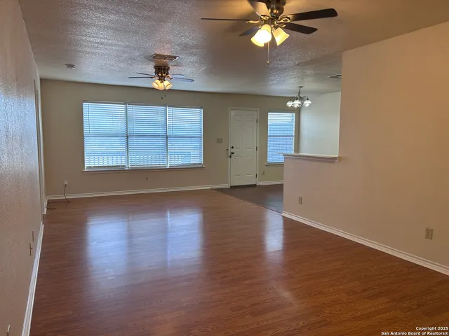 an empty room with wooden floor chandelier fan and windows
