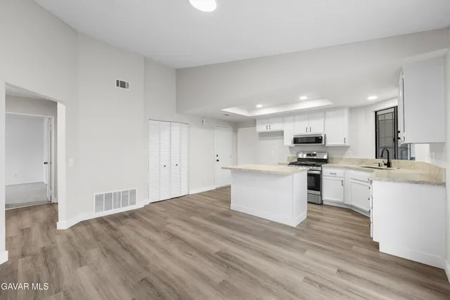 a view of kitchen with stainless steel appliances granite countertop a stove top oven a sink with white cabinets and wooden floor