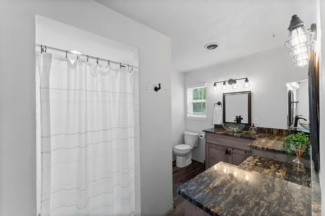 a spacious bathroom with a granite countertop sink a toilet a mirror and shower