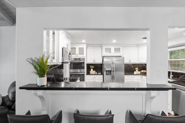 a kitchen with stainless steel appliances granite countertop a refrigerator a stove and white cabinets with wooden floor