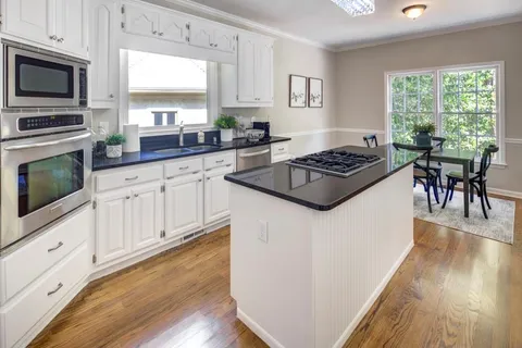 a kitchen with granite countertop a stove top oven a sink dishwasher a dining table and chairs with wooden floor