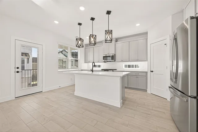 a kitchen with stainless steel appliances kitchen island granite countertop a refrigerator a stove and white cabinets with wooden floor