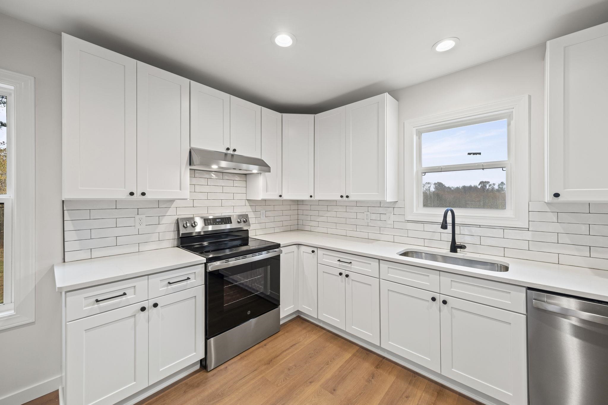 835 Curve Woodville Road Gates, TN 38037 - Photo 10 of 30 Kitchen featuring appliances with stainless steel finishes, white cabinetry, light wood-style flooring, under cabinet range hood, and light stone countertops