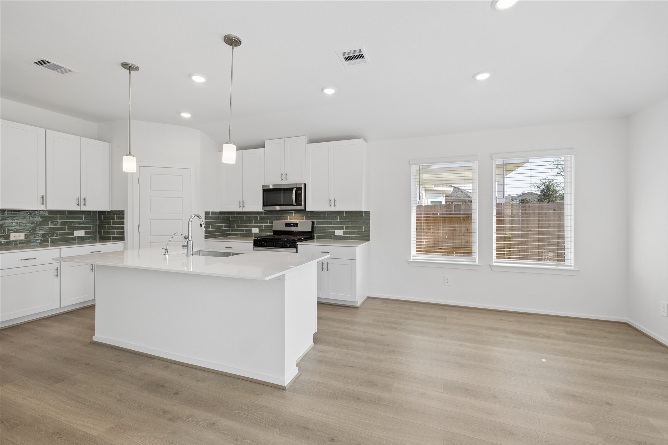 Discover culinary bliss in this bright, modern kitchen featuring sleek white cabinetry, a spacious island with elegant pendant lighting, and a chic subway tile backsplash.