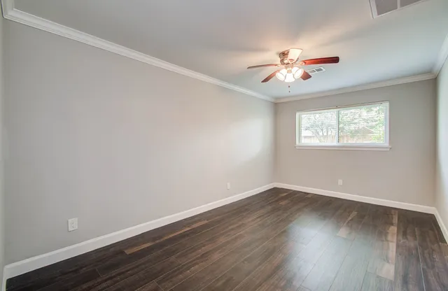 an empty room with wooden floor fan and windows