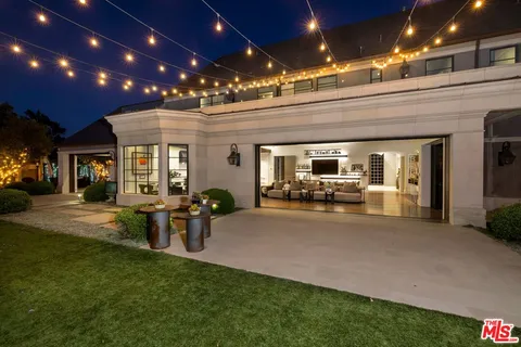 a view of a patio with couches table and chairs under an umbrella with large trees