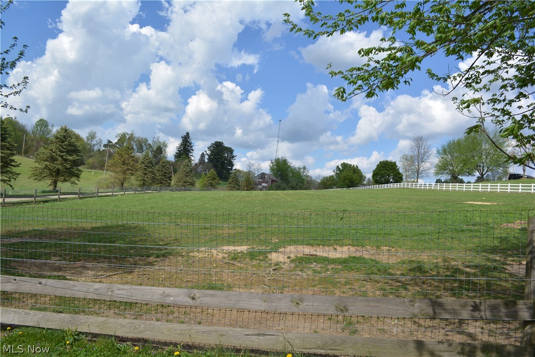 2363 Tabor Ridge Road Northeast New Philadelphia, OH 44663 - Photo 16 of 42 Expansive green pasture framed by a wooden and wire fence, featuring distant white fencing and mature trees
