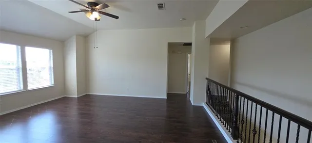 an empty room with wooden floor fan and windows