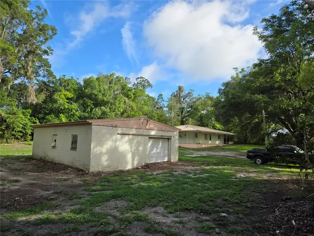 a view of a small white house with a yard and a large tree