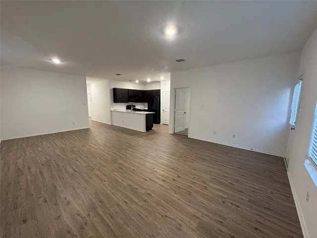 an empty room with wooden floor a kitchen view and windows