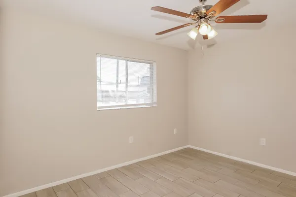 an empty room with wooden floor chandelier fan and windows