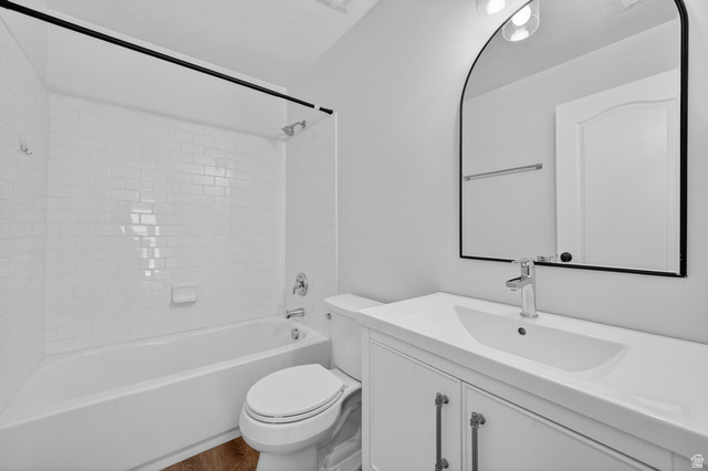 14771 Haddington Road Draper, UT 84020 - Photo 24 of 44 Bathroom featuring a white subway tile tub surround, white vanity with integrated sink, chrome faucet, arched mirror, and wood-finish flooring