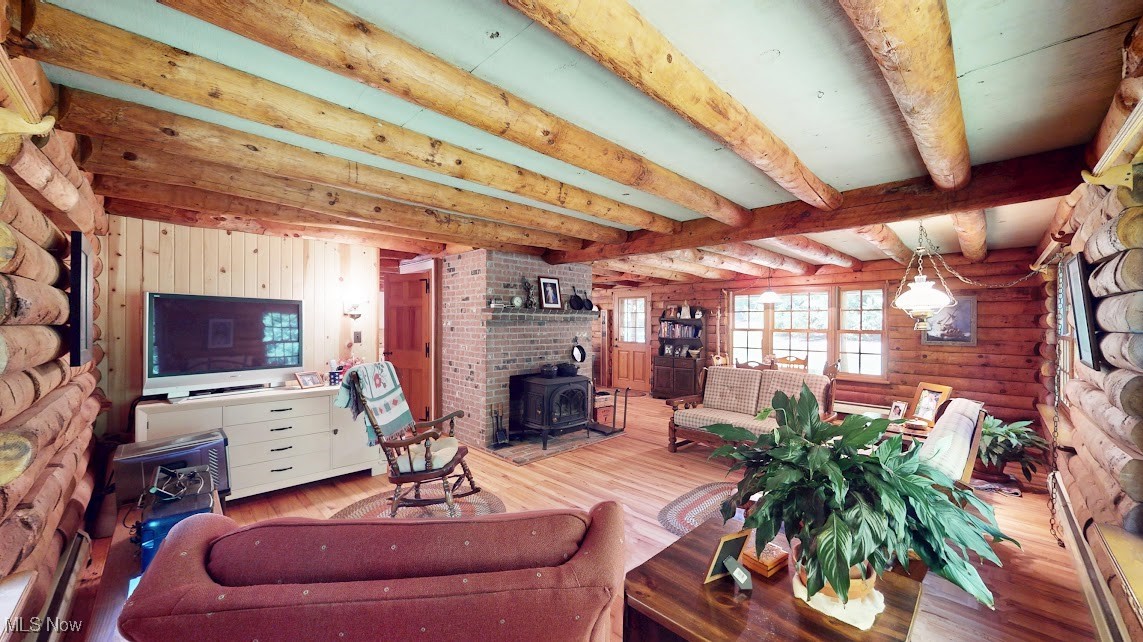 9471 Sherman Road Chesterland, OH 44026 - Photo 11 of 40 Living room featuring a wood stove, beam ceiling, wood finished floors, rustic walls, and baseboard heating