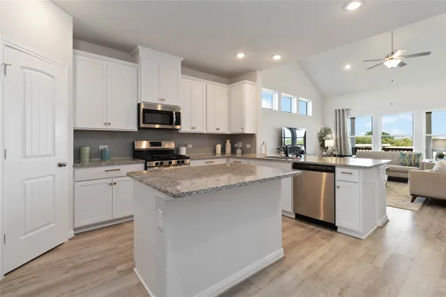 a kitchen with stainless steel appliances granite countertop a refrigerator a stove top oven a sink dishwasher and white cabinets with wooden floor