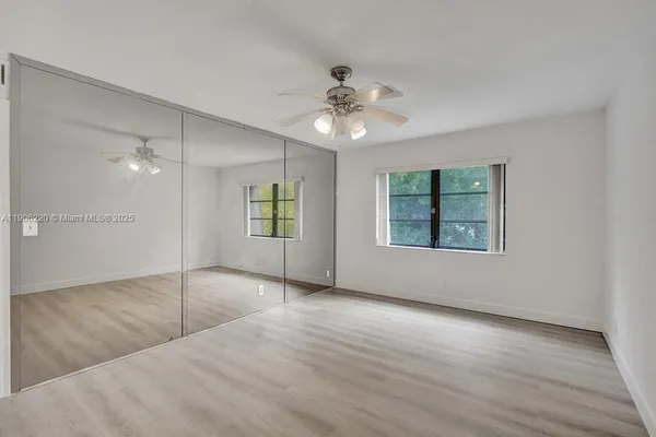 an empty room with wooden floor chandelier fan and windows