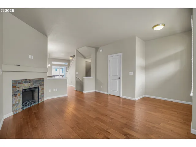a view of an empty room with wooden floor fireplace and a window