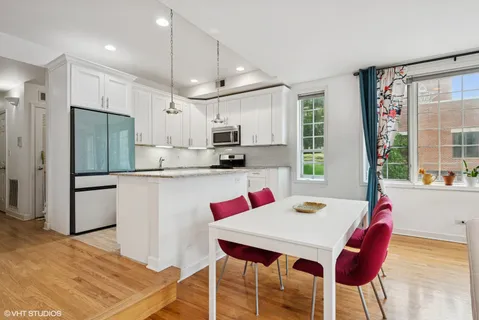 a kitchen with stainless steel appliances kitchen island granite countertop a dining table chairs and a refrigerator